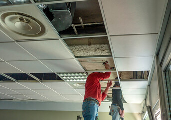 Construction worker assemble a suspended ceiling with drywall and fixing the drywall to the ceiling...