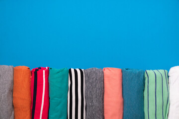 close up of rolled colorful t shirt clothes on blue table background, lifestyle concept