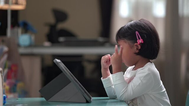 Small Asian girl sitting at table studying online.