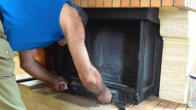 A man lays down an empty ash tray in an empty open fireplace.