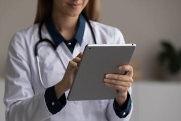 Close up young female general practitioner doctor medical worker holding digital computer tablet in hands, web surfing information or giving distant healthcare advice, modern technology and medicine.