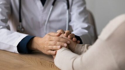 Close up kind compassionate young woman holding hands of stressed old senior retired female patient, showing support or comforting telling health test results at checkup meeting in clinic office.