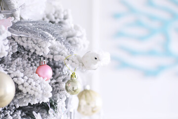 Christmas holiday background. Silver and color bauble hanging from a decorated on tree with bokeh and snow, copy space.