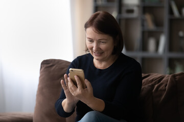 Joyful middle aged elderly woman using smartphone software applications, playing mobile games, reading media news online, communicating distantly in social networks or shopping in internet store.