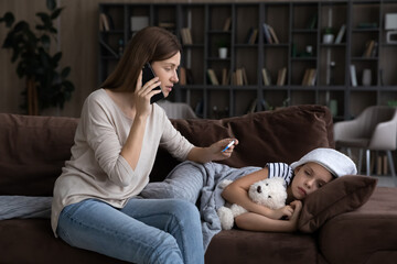 Anxious young mother calling doctor, taking healthcare advices, worrying about ill small child daughter. Nervous millennial mum consulting by phone call with pediatrician, sitting near sick kid.