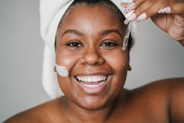 African young woman applying face serum and skin mask beauty treatment on her face - Focus on...