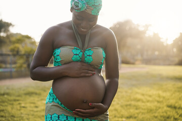 Happy african pregnant woman touching her belly outdoor - Focus on hands 