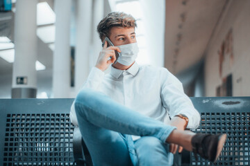 Hombre joven llamando por telefono en la estación de transporte cumpliendo el distanciamiento...