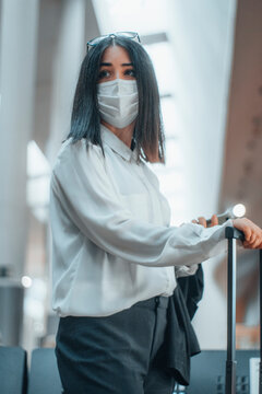 Mujer joven esperando con mascarilla en la estaci&oacute;n de tren junto a su equipaje
