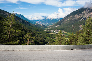 Carretera por los alpes franceses con un valle alpino al fondo  y las fortalezas de Briançon