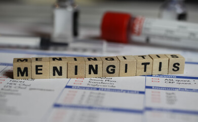 Viersen, Germany - June 1. 2021: Closeup of word meningitis on laboratory requisition slip with syringe and vial