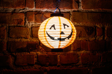 Smiling glowing jack-o-lantern hanging on old red brick wall at night. Halloween decoration concept