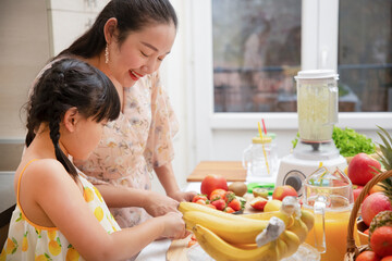 Obraz na płótnie Canvas Happy asian family mother and her daughter enjoy prepare freshly squeezed fruits with vegetables for making smoothies for breakfast together in the kitchen.diet and Health concept.