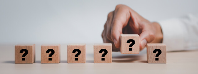 Hand hold Wooden cube block in question mark mean what on cement table background, column of wooden blocks with question sign mark. copy space,FAQ frequently asked questions, Answer, Information
