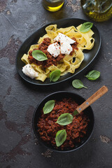 Pappardelle pasta with bolognese sauce and mozzarella cheese, vertical shot on a brown stone background, high angle view