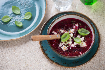 Beetroot and quinoa soup topped with bryndza and served in a turquoise bowl, elevated view on a beige marble background, horizontal shot