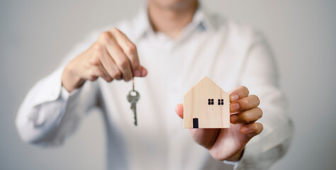 The concept of moving to a new home, Hand holding wooden house and home key, Property investment and house mortgage financial real estate, Real estate agents hold the keys to the wooden house