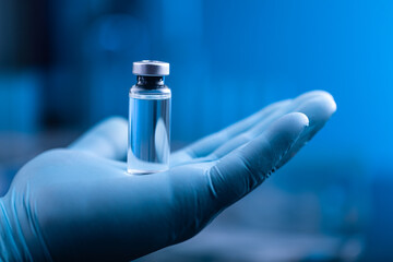 The hand of a scientist or doctor holds a bottle of serum drug for injections