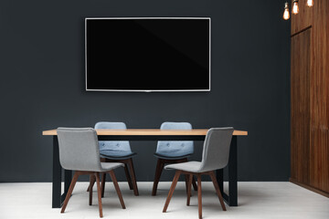Modern wide screen TV on black wall in room with stylish furniture