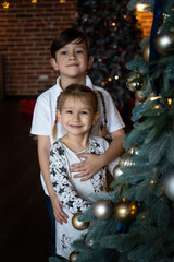Merry Christmas and Happy Holidays. Cute little child girl and boy is decorating the Christmas tree indoors.