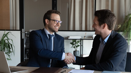 Smiling businessman manager in glasses shaking satisfied client hand at meeting, closing successful...