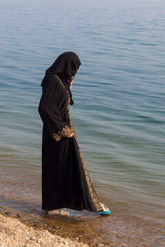 A Muslim woman in national clothes wets her feet the sea.