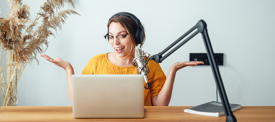 Young woman recording podcast on his laptop computer with headphones and  microphone. Female...