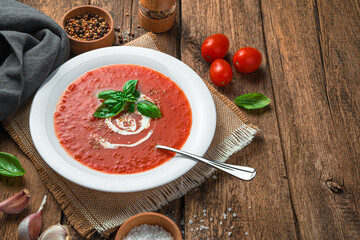 Homemade tomato soup with basil and cream on a wooden background. Healthy, organic food. Side view, space for copying.