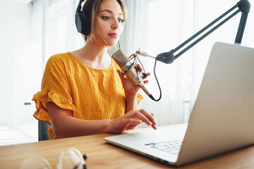 Female podcaster recording her podcast using microphone and laptop at his home broadcast studio....