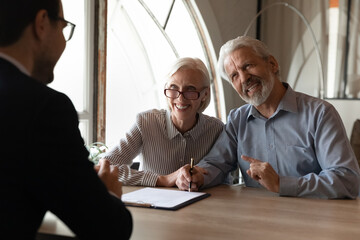 Excited mature couple signing agreement contract at meeting with manager, happy overjoyed senior...