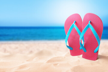 Fototapeta na wymiar Pink flip flops in sand on sandy beach near sea. Space for text
