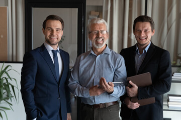 Portrait of three smiling confident businessmen employees startup team with mature executive standing in office, businesspeople workers coworkers group looking at camera, posing for corporate photo