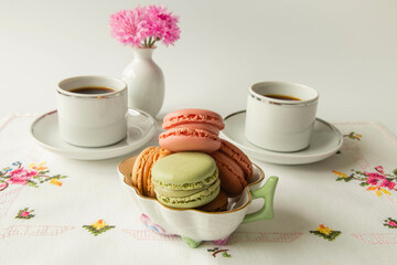 Cups of coffee and macaroons with flowers in a vase on a white handcrafted tablecloth with cross stitched flowers 