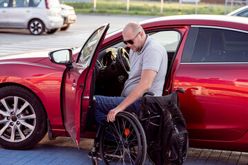 Young handicapped driver getting in red car fom wheelchair