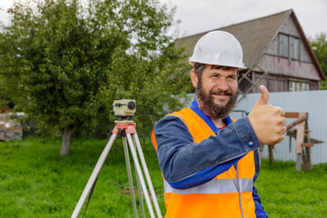 A civil engineer with an optical level approves the work of his colleagues with a smile by raising his hand.