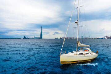 Fototapeta premium Sailboat in the Gulf of Finland, Baltic Sea. Dramatic clouds and sky, storm clouds over sea. Residential areas and Lakhta in St. Petersburg in the background