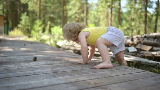 Little funny cute blonde girl child toddler in yellow undershirt and grey shorts walking playing on wooden eco trail outside at summer at front yard countryside. Healthy happy childhood concept. 