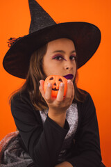 Studio portrait of a little witch with a little pumpkin in her hand on Halloween