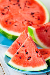 Ripe red sliced watermelon pieces on blue plates on wooden background. Concept of delicious vegan low calories summer sweet desserts. White wooden background. Close up macro