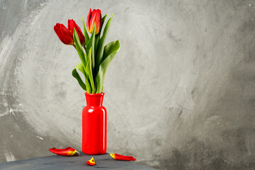 fallen tulip petals on the table. red vase with three flowers