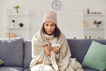 Woman with a runny nose sits in front of the webcam on the couch wrapped in a plaid and hat. Sick...