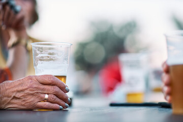 Close up of an old woman's hand holding a glass of beer. - obrazy, fototapety, plakaty