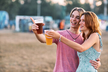 A young couple in love is hugging and holding a beer. They are pointing at something interesting. - obrazy, fototapety, plakaty