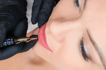Young woman having permanent makeup on her lips at the beauticians salon.