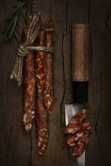 Smoked hunter sausages and slices on knife's blade continuing shape of it with rosmarine on wooden background