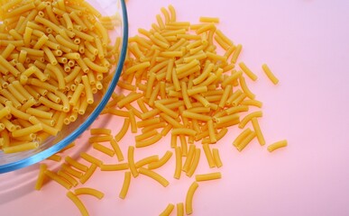 Uncooed pasta in a bowl, top view, color background