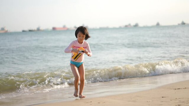 Asian Chinese girl daughter child playing with plastic toy excavator by the sea