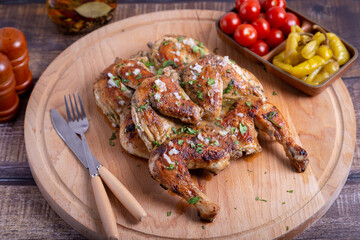 Tapaca (tabaca) chickens with cherry tomatoes, pepperoni and garlic and cilantro on a wooden board. Traditional Georgian dish. Close-up.
