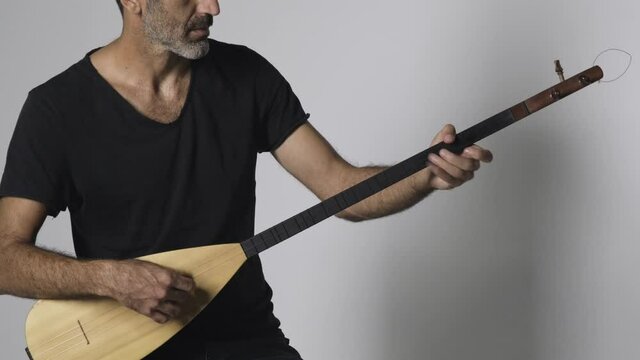 Middle eastern man playing Kopuz which is a string instrument named Baglama with three strings on a white background.