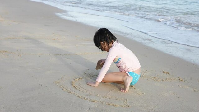 
Slow motion little asian Chinese girl daughter playing at the beach drawing on sand waves sea